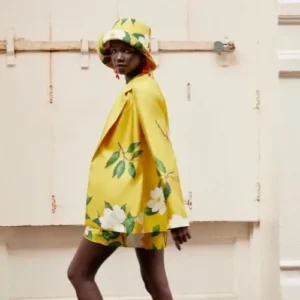 Mujer vistiendo un conjunto floral amarillo con chaqueta, shorts y sombrero a juego, diseño de Oscar de la Renta de la colección 2022, destacando un estilo vibrante y elegante.