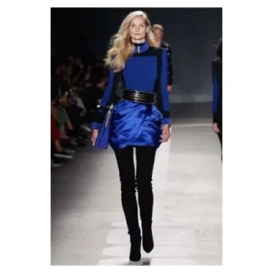 Modelo desfilando con un diseño de Balmain en tonos azul eléctrico y negro, con detalles satinados y cinturón metálico, reflejando sofisticación y vanguardia.