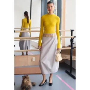 Modelo con un conjunto de Tory Burch compuesto por un suéter amarillo vibrante y una falda gris amplia, resaltando el estilo elegante y contemporáneo de la marca.
